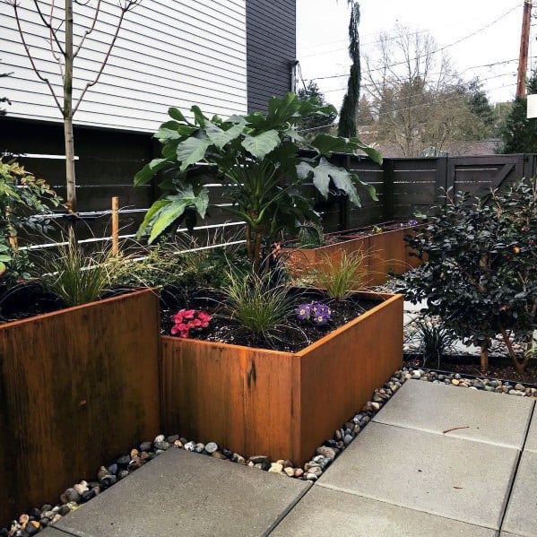 Modern garden with steel planters, vibrant plants, and stone edging, complementing a well-maintained walkway