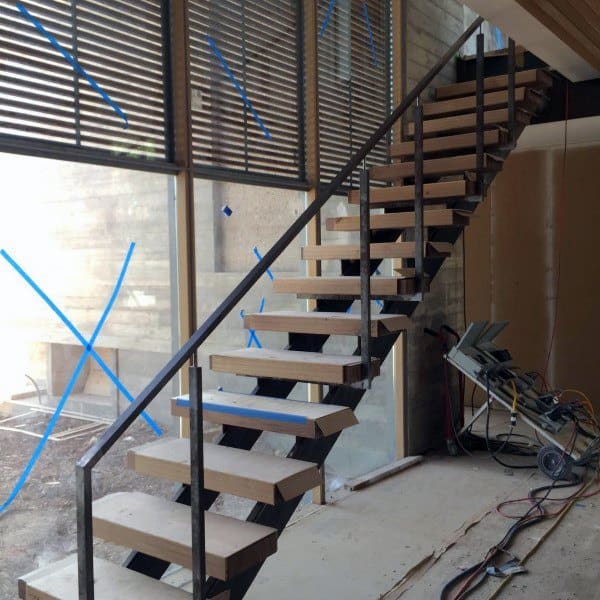 Modern floating staircase with wooden steps stands amidst construction materials in an unfinished room