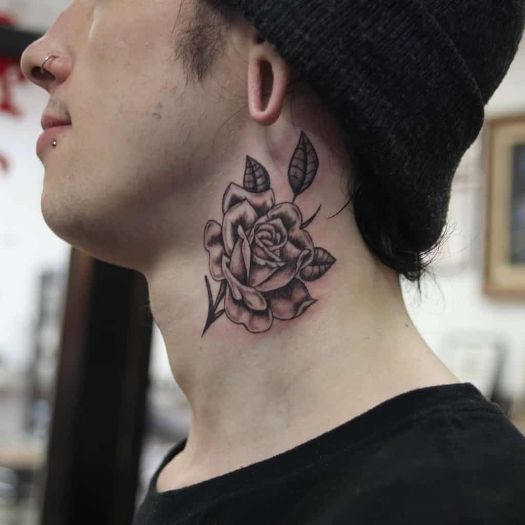 Black and grey shaded rose tattoo on the side of the neck, showcasing intricate details with leaves and a stem for a bold yet elegant design