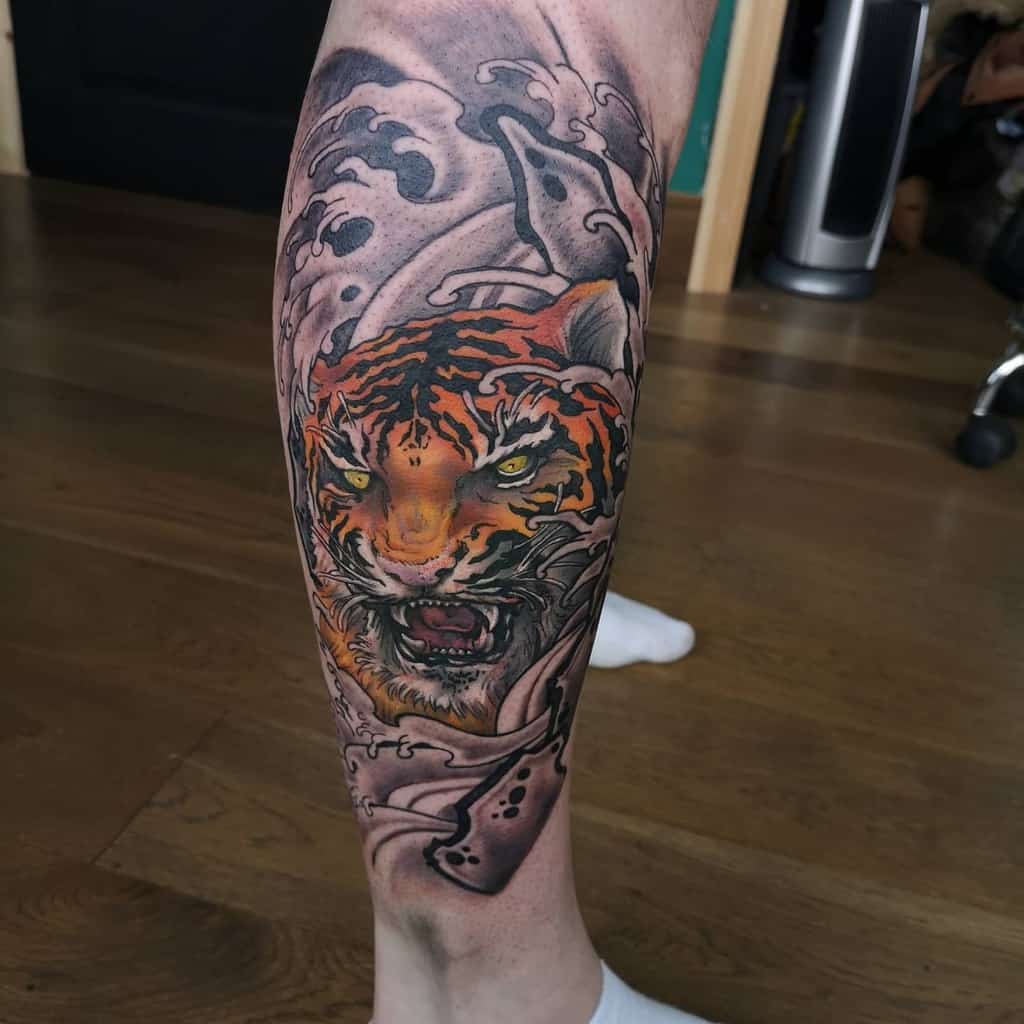 A leg sleeve tattoo of a tiger head with an open mouth surrounded by waves 