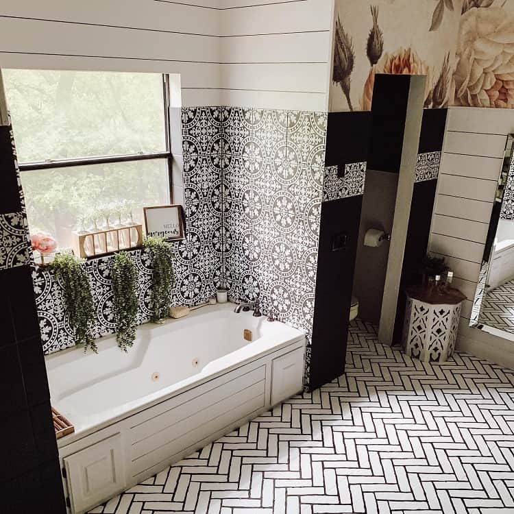 Farmhouse bathroom with patterned wall tiles, herringbone floor, built-in tub, and greenery.