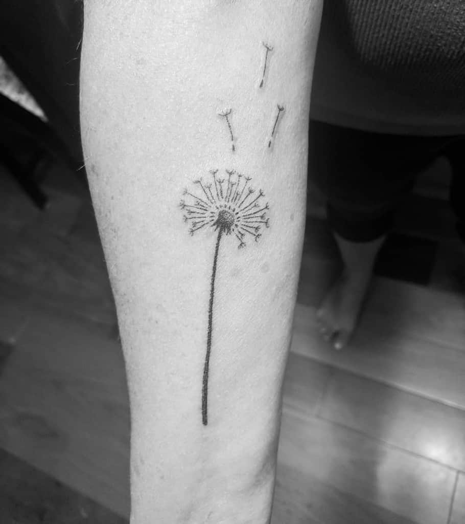 This image features a beautiful minimalist dandelion tattoo on the forearm, capturing the delicate and whimsical nature of the dandelion seeds as they drift away.