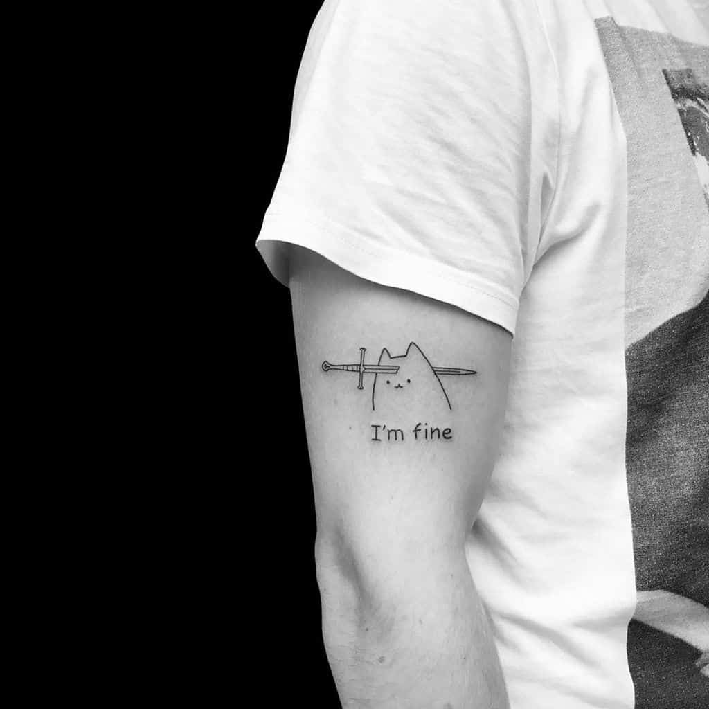 A minimalist black ink tattoo of a stabbed cartoon mountain with the words 'I'm fine,' blending humor with a melancholic touch on the upper arm.