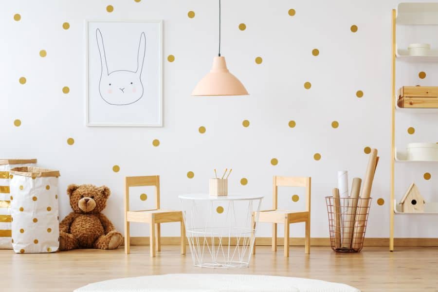 Children's room with an accent wall of polka dots, teddy bear, small table, chairs, and framed rabbit artwork