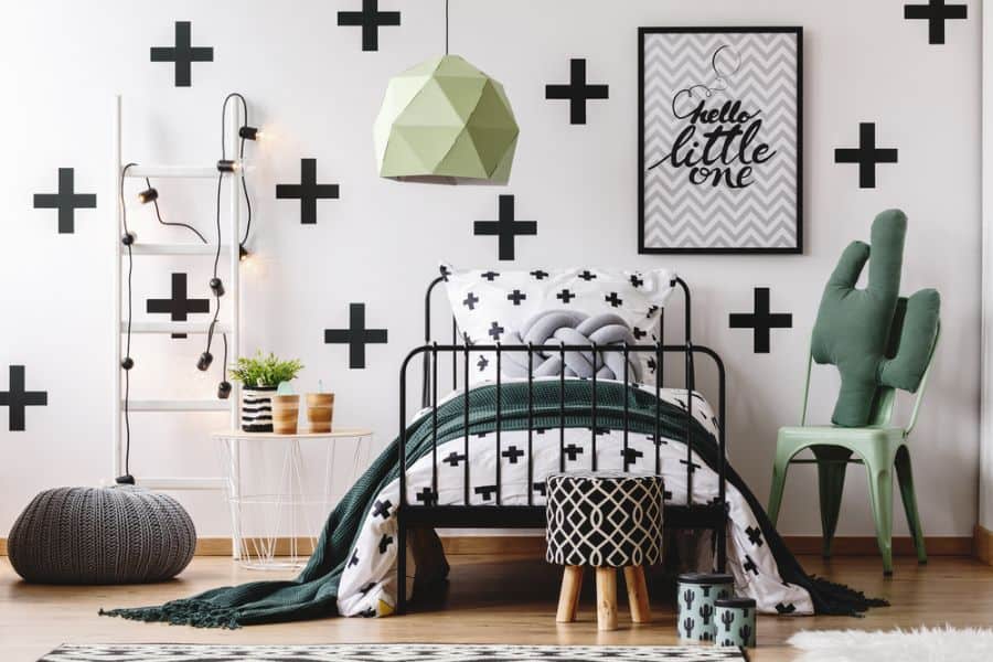 Contemporary kids' bedroom with an accent wall, geometric decor, black cross accents, green chair, and a cactus lamp