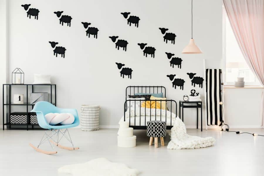 Minimalist bedroom with black sheep decals on an accent wall, single bed, blue chair, and soft lighting