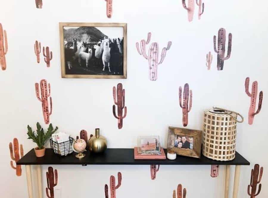 Shelf with decorative items against an accent wall featuring pink cactus patterns and a framed photo of llamas