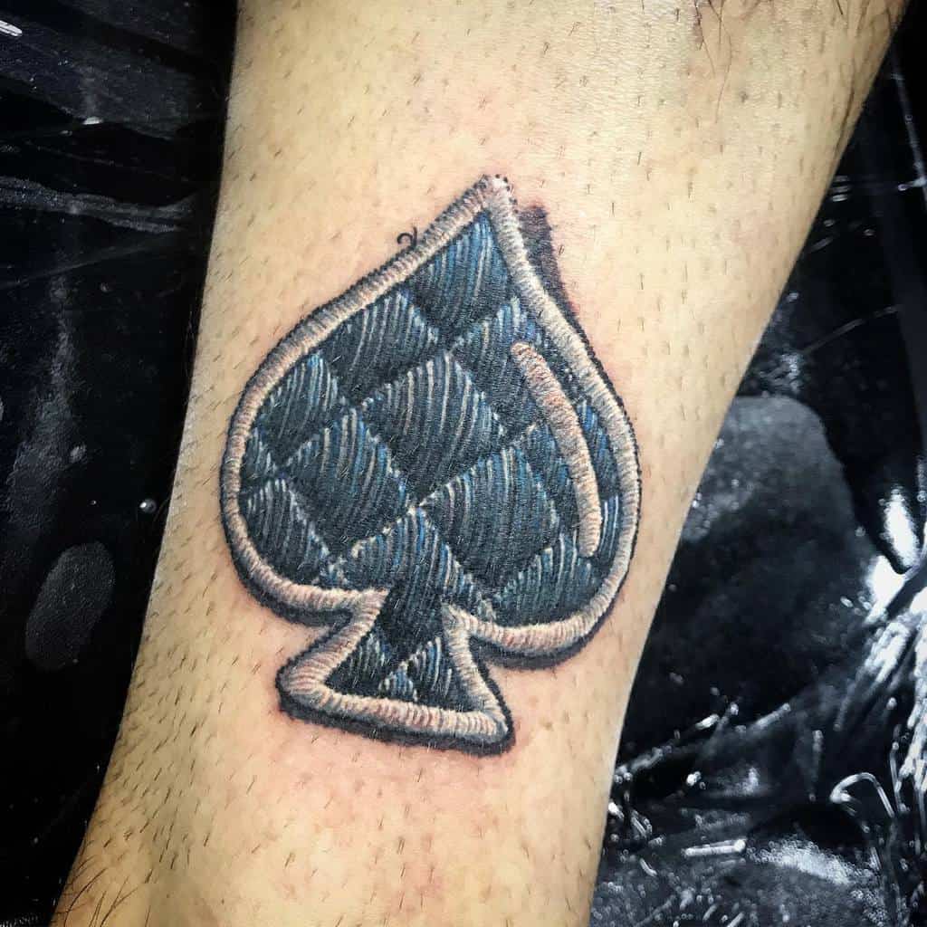 A tattoo of the Ace of Spades symbol designed to look like quilted fabric, with a stitched border