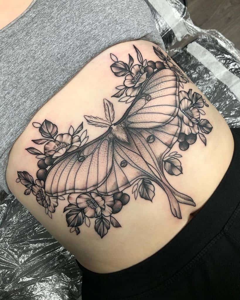 A black and grey Luna Moth tattoo, surrounded by flowers and detailed shading