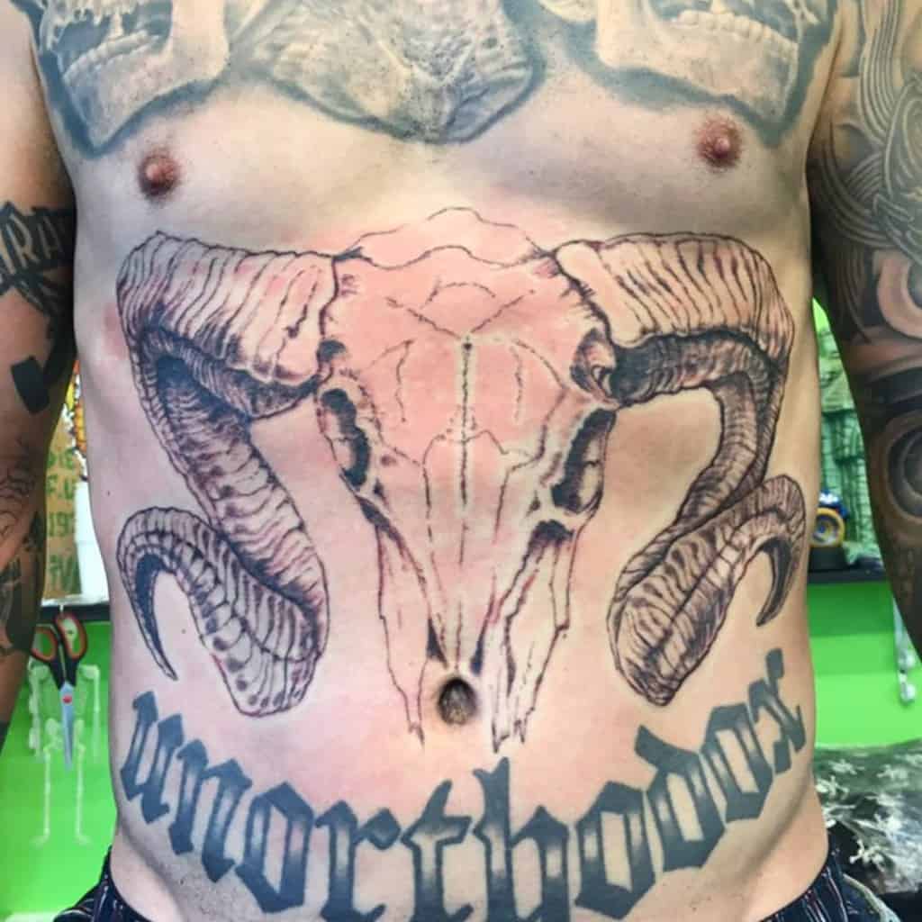 Man with a prominent ram skull tattoo on stomach and "unorthodox" text inked below