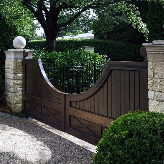 Dark wood estate gate with curved tops and stone columns for a classic, elegant entry.