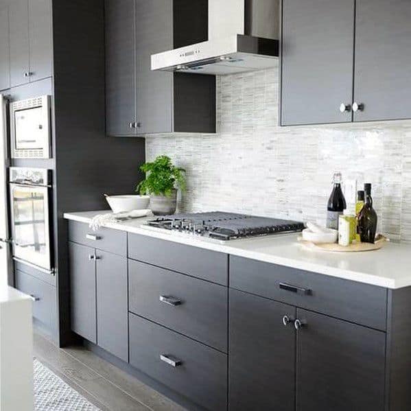 Modern kitchen with sleek dark cabinets, a textured light stone backsplash, and minimalist stainless steel appliances