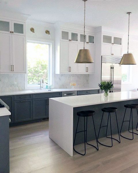 Bright kitchen with a hexagonal stone backsplash, two-tone cabinetry, a long island, and gold pendant lighting