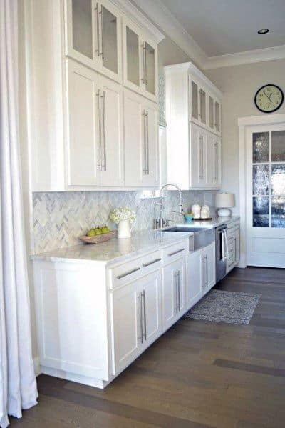 Airy kitchen with white cabinetry, a subtle herringbone stone backsplash, sleek hardware, and light wood flooring