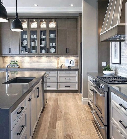 Modern kitchen with a sleek stone backsplash, two-tone cabinetry, stainless steel appliances, and industrial pendant lighting