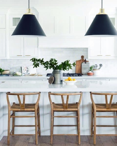Bright kitchen with a subway tile backsplash, wooden bar stools, bold black pendant lights, and a white quartz island