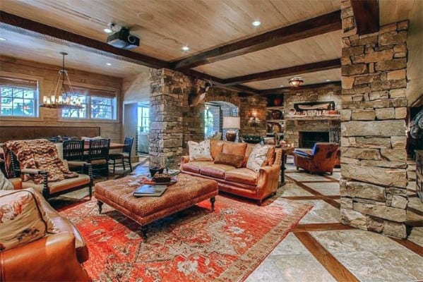 Rustic design featuring stone columns, exposed wooden beams, leather couches, and a red patterned rug.