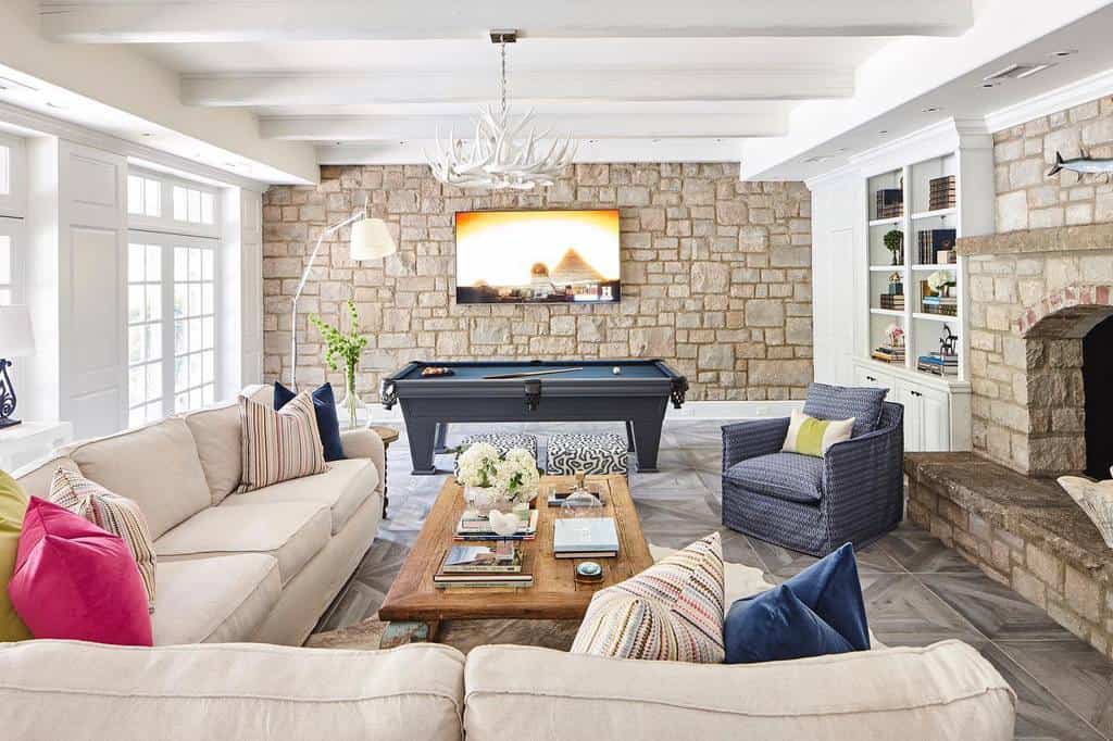 Living room with stone walls, pool table, and cozy seating around a rustic fireplace.