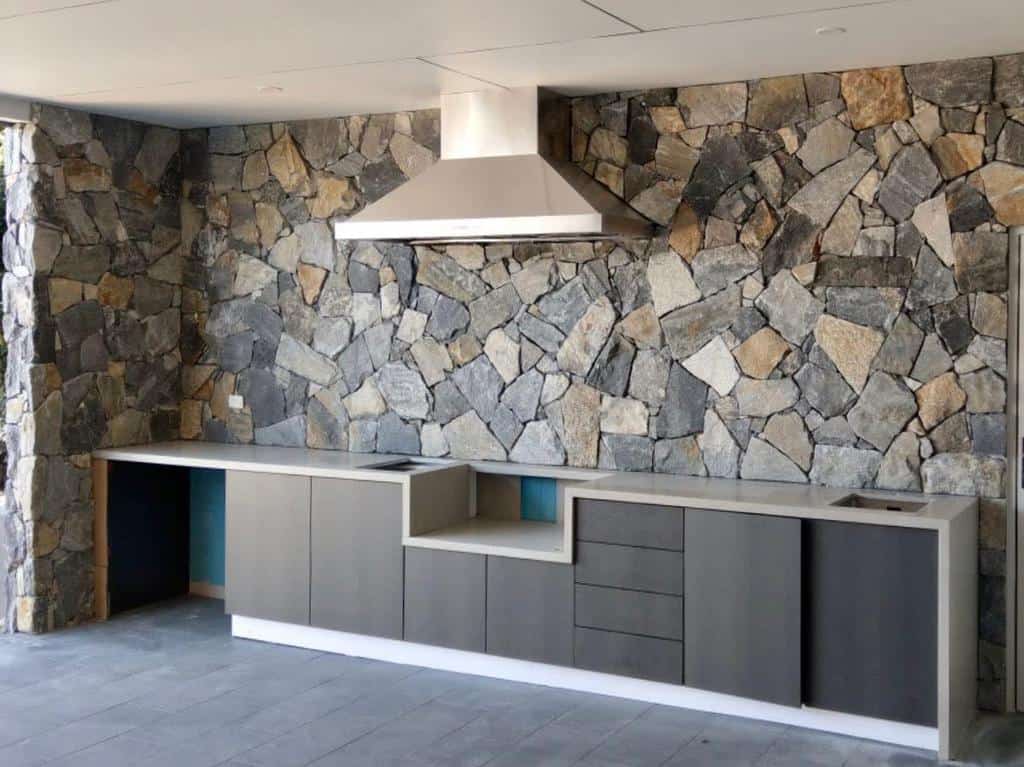 Modern kitchen with unfinished stone walls and sleek cabinetry.