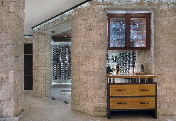 Elegant wine cellar with stone walls, glass rack, and wooden cabinet. Rows of wine bottles complete the scene