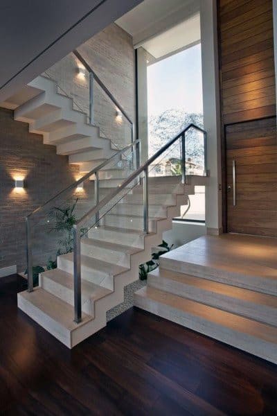 Modern staircase with wooden steps, glass railing, wall lights, and a large window framing an outdoor tree