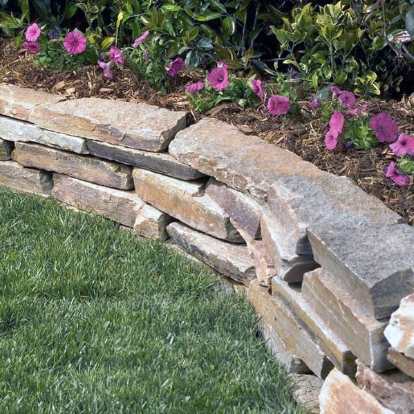 A curved stone border around a garden bed, featuring vibrant flowers and lush grass, adding structure to the landscape