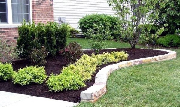A curved stone border around a flower bed, featuring neatly arranged plants and mulch, enhancing the home's landscape