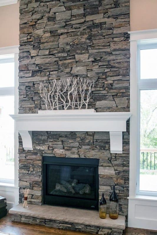 Rustic stacked-stone fireplace with a white mantel and symmetrical windows, blending traditional and modern elements.