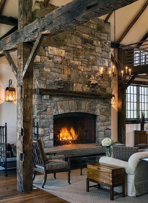 Rustic living room with a large stone fireplace, exposed wooden beams, lantern-style wall lights, and cozy seating.