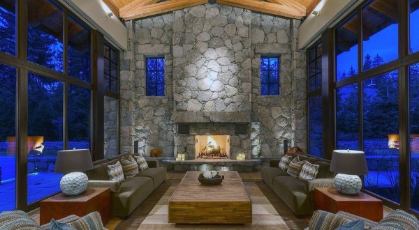 Spacious living room with tall stone fireplace, vaulted ceiling, and large floor-to-ceiling windows.