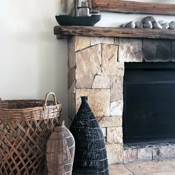Cozy fireplace featuring natural stonework, a rustic wooden mantel, and decorative wicker and woven baskets.