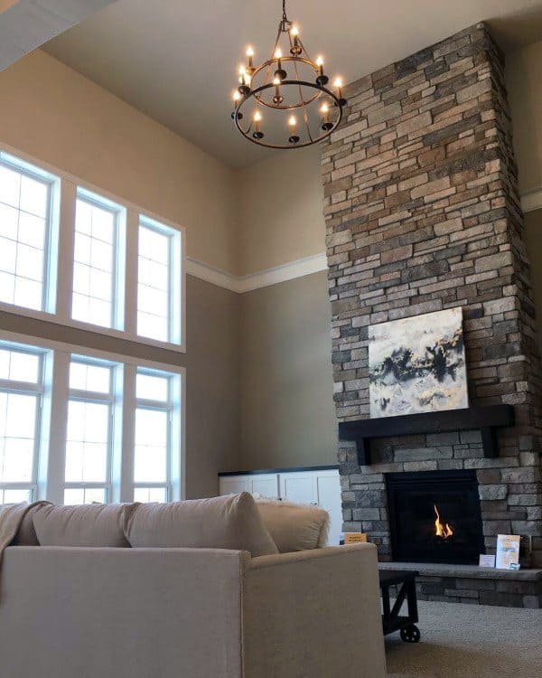 Modern living room with tall stone fireplace, abstract art, and large grid-style windows.