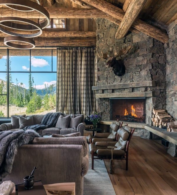 Cozy living room with a grand stone fireplace, wooden beams, and panoramic forest views.