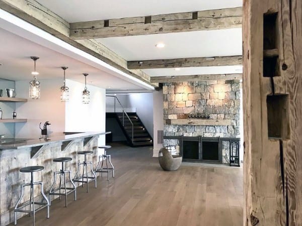 Open-concept living space featuring a rustic stone fireplace, exposed wood beams, and a modern bar area.