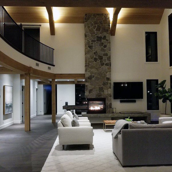 Contemporary living room featuring a tall stone fireplace, exposed wooden beams, and a cozy seating arrangement with neutral tones.
