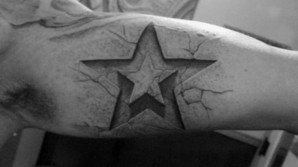 3D star tattoo on inner bicep with a carved stone effect and cracked surface, creating a rugged and deeply etched look.