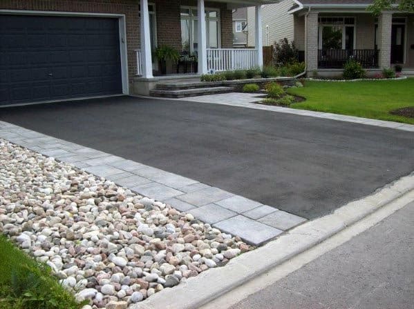 Asphalt driveway with gray stone edging and a pebble border next to a landscaped front yard.