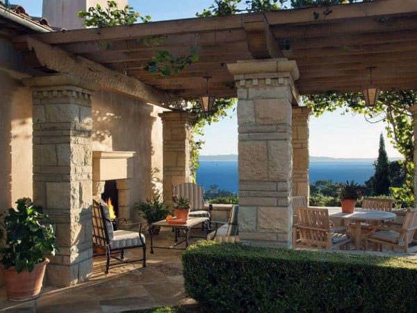 Elegant pergola with stone pillars, wooden beams, a cozy fireplace, and stunning ocean views.