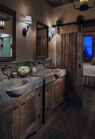 Rustic bathroom with wooden cabinets, dual sinks, dim lighting, and a sliding door slightly open