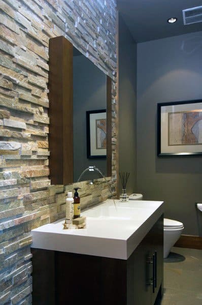 Modern half bath with a stone accent wall, large mirror, and minimalist sink, art frames on the gray wall