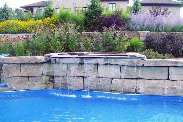 Backyard pool with waterfall feature, surrounded by lush garden and stone wall