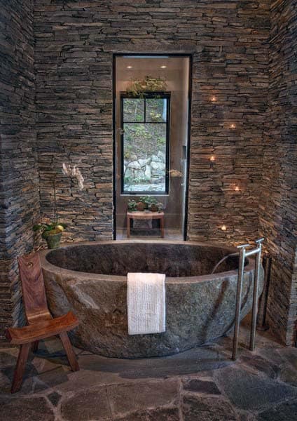 Rustic stone bathtub in bathroom with stacked stone walls and narrow window