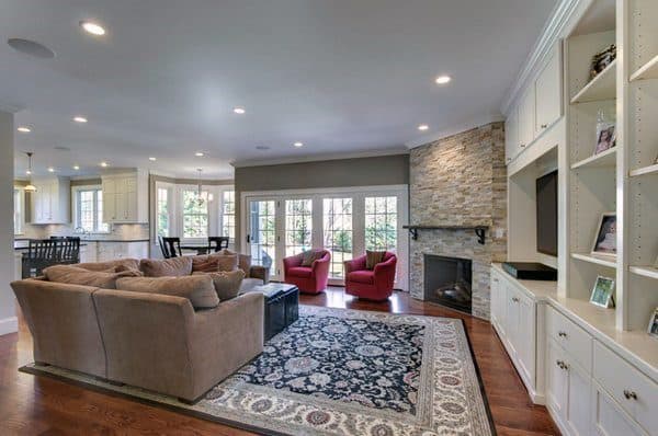 Open living room with stone corner fireplace, built-in white bookcases, and beige sectional sofa.