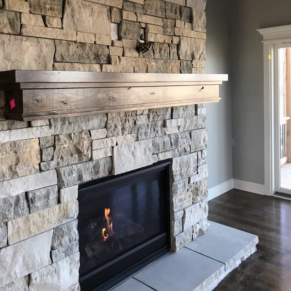 Gas fireplace with a black frame, rustic stone surround, and wooden mantle beam.