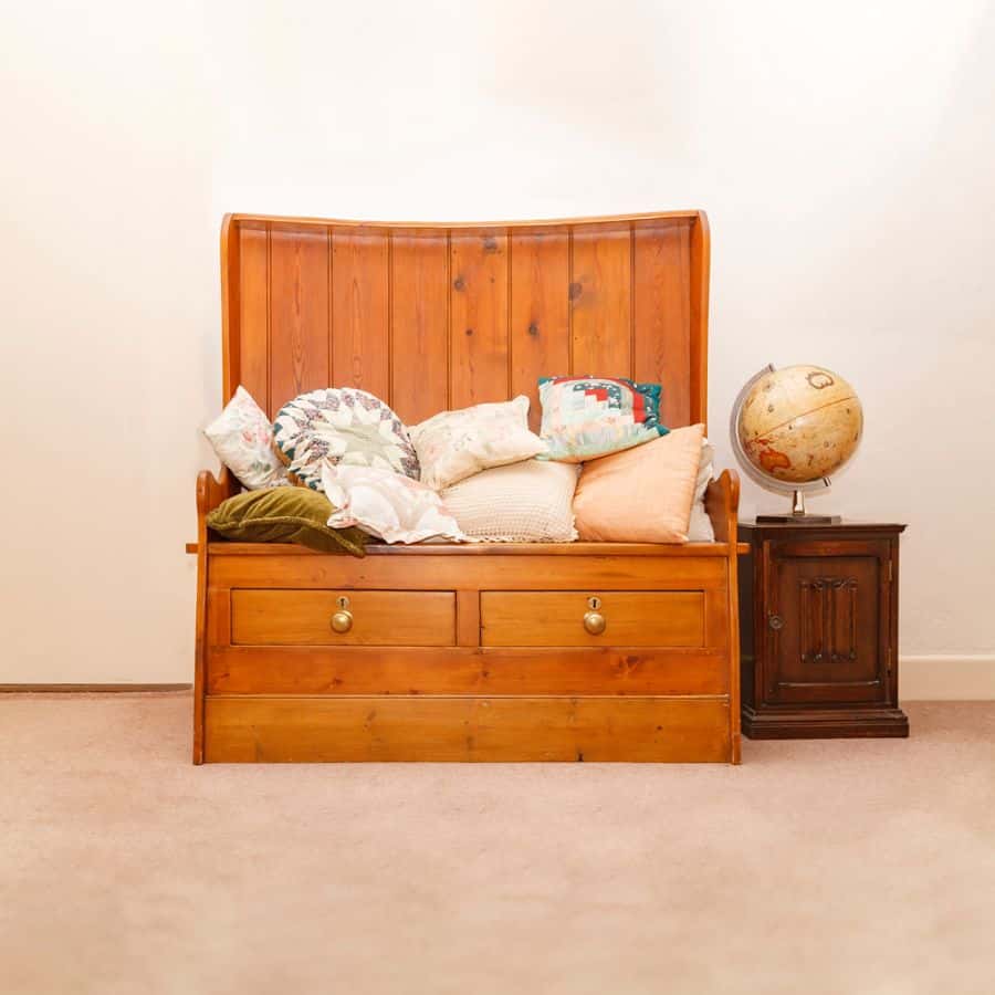 Wooden bench with storage drawers and decorative pillows, next to a vintage globe.