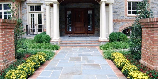 Elegant front entrance with a brick walkway, lush flowers, and symmetrical columns leading to a classic wooden door