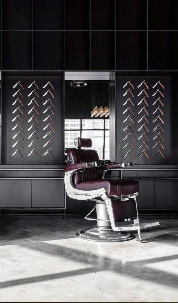 Minimalist barbershop with dark walls, straight razor decor, and a burgundy leather chair.
