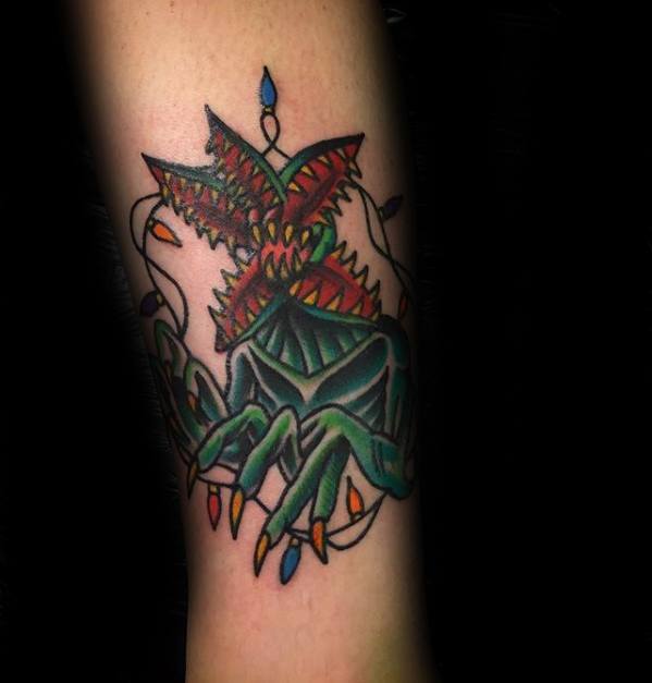 Colorful traditional-style tattoo of the Demogorgon with sharp teeth and claws, tangled in glowing Christmas lights from Stranger Things.