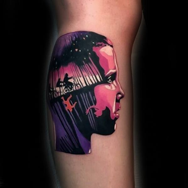 Vibrant Stranger Things tattoo of Eleven’s side profile with silhouettes of kids biking and a figure falling into the Upside Down inside.