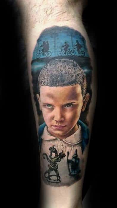 Realistic Stranger Things tattoo of Eleven with intense gaze, featuring kids biking above and the Demogorgon and lamp on her dress below.